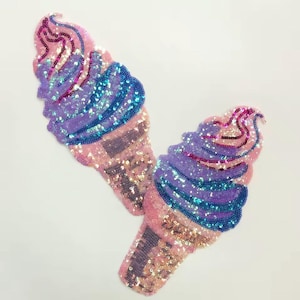 May include: Two ice cream cone patches covered in shimmering sequins. The soft serve portion features swirling layers of light purple and bright blue sequins, while the cone section is crafted with light pink and gold-toned sequins.