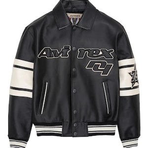 May include: A black faux leather varsity jacket featuring a pointed collar, snap button closure, and two front pockets. The chest displays the text Avirex in white and black. Each sleeve has two white stripes and a star patch with the number 75.