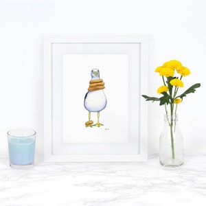 May include: A white framed print of a watercolor painting of a seagull wearing a stack of three yellow life preservers. The seagull is standing on a white background.