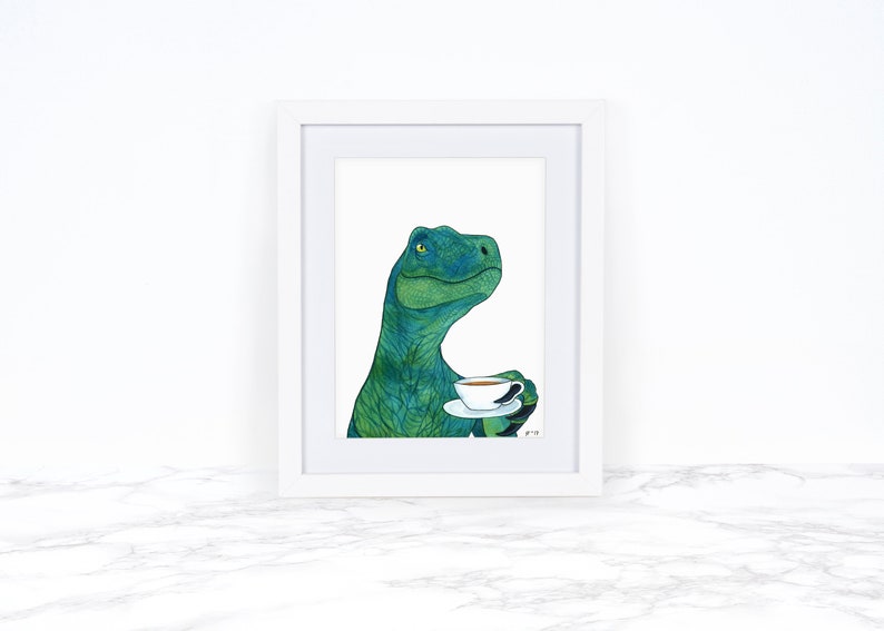 May include: A framed illustration of a green dinosaur holding a white teacup with a saucer. The dinosaur has a green and blue patterned body and is looking to the right. The background is white.