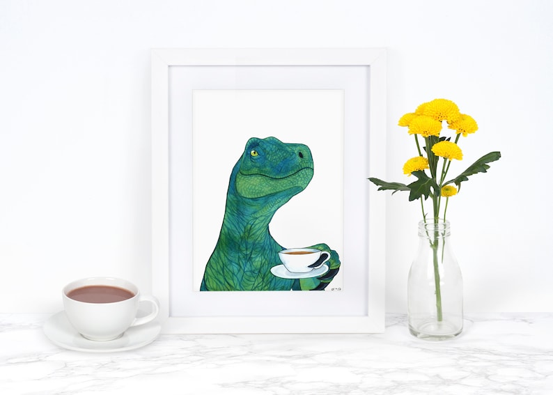 May include: A framed illustration of a green dinosaur holding a cup of tea. The dinosaur is looking to the right and has a thoughtful expression. The illustration is on a white background and is framed in a white frame.