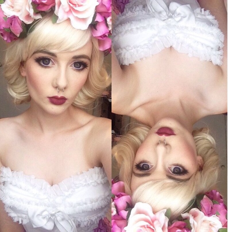 Puede incluir: Imagen dividida que muestra a una persona con cabello rubio y una corona floral. La persona lleva una parte superior blanca con detalles de volantes y un lazo. El maquillaje incluye l&aacute;piz labial oscuro y sombra de ojos. La imagen est&aacute; dividida, un lado vertical y el otro invertido.