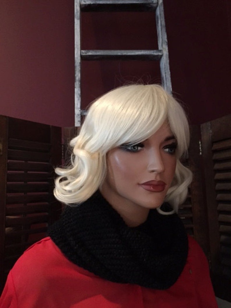 Puede incluir: Una cabeza de maniqu&iacute; con una peluca rubia y maquillaje de ojos oscuro. El maniqu&iacute; lleva un cuello de punto negro y una parte superior roja. Una escalera blanca desgastada est&aacute; en el fondo.