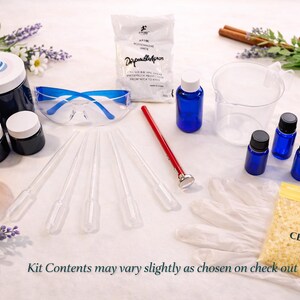 May include: A candle making kit featuring a large dark blue jar, two small dark blue jars, blue safety glasses, a white apron, a red thermometer, five plastic pipettes, a clear measuring beaker, six small blue bottles, and a bag of wax beads labeled CEB-N.