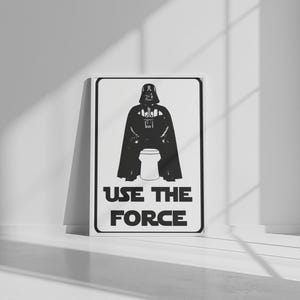 Può includere: Un poster rettangolare bianco con un'illustrazione grafica nera di una figura con casco e mantello seduta su un water. Sotto la figura, il testo recita USE THE FORCE in lettere maiuscole nere, racchiuso entro un sottile bordo nero.