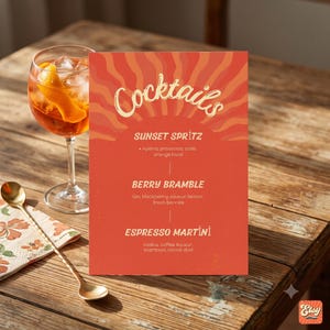 May include: A rectangular cocktail menu card with a red background and orange sunburst graphic. The text reads Cocktails, Sunset Spritz, Berry Bramble, and Espresso Martini with ingredient lists. A glass of orange cocktail sits to the left.