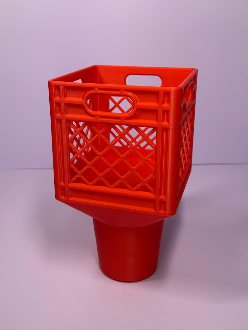 May include: A bright orange plastic cup holder featuring a square, crate-style top section with a lattice pattern and integrated handles, transitioning into a solid, tapered cylindrical base designed to hold a beverage container securely.