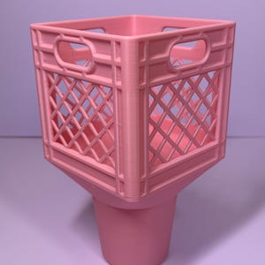 May include: A light pink plastic storage container featuring a square, open-grid crate top with integrated handles on each side, seamlessly connected to a solid, tapered cylindrical base, creating a singular, unified desk organizer structure.