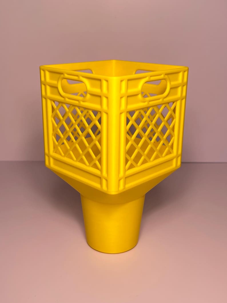 May include: A bright yellow plastic container featuring a square, open-top crate design with a diamond-patterned lattice structure on the sides and integrated handles, transitioning into a solid, tapered cylindrical base at the bottom.