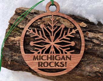 May include: A wooden Christmas ornament with a snowflake design and the text "MICHIGAN ROCKS!" hanging on a piece of tree bark.