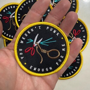 May include: A circular embroidered patch with a black background and a bright yellow border. The design features a pair of scissors with red handles and a brown rope loop. The text "YOU WEREN'T PUNK ENOUGH FOR ME" is stitched in white around the edge.