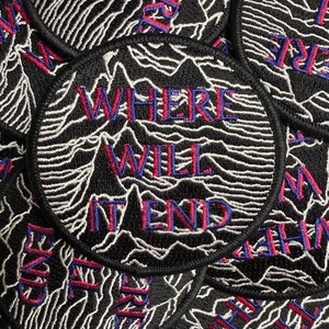 May include: A circular embroidered patch featuring a black background with white topographic line patterns. The text WHERE WILL IT END is stitched in red with blue outlines across the centre of the patch, which has a black merrowed border.