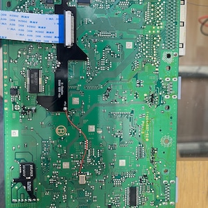 May include: A green printed circuit board featuring an X-Station 550X QSB v1b module, a blue ribbon cable labeled AWM 20624 80C 60V VW-1, a red wire connection, and a black X-Reset 550X QSB v1 component, with the text 1-664-537-520 PU-18 printed on it.