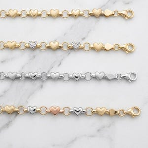 May include: Four bracelets featuring a repeating heart-link design connected by small circular rings. The top bracelet is yellow gold, the second is yellow gold with textured hearts, the third is silver, and the bottom is a mix of gold, silver, and rose gold.