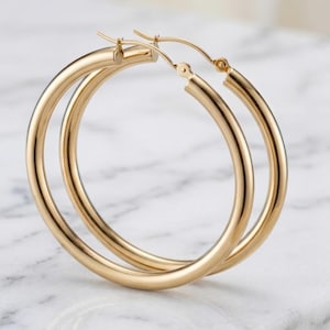 May include: A pair of polished gold hoop earrings with a smooth, rounded tubular design. The earrings feature a hinged post mechanism at the top, allowing them to open and close securely. The metal has a bright, reflective finish throughout.