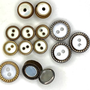 Può includere: Assortimento di bottoni bianchi e dorati con due, tre e quattro fori. Alcuni bottoni hanno un bordo decorativo.