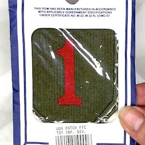 Puede incluir: Un parche militar verde y rojo con el número "1" en él. El parche está etiquetado como "USA PATCH F/C 1ST INF. DIV." y tiene un código de barras y una etiqueta de precio de 2,30 €.