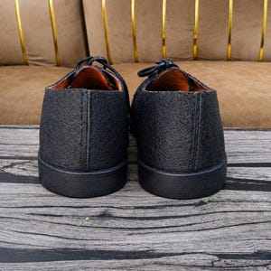 K&ouml;nnte beinhalten: Ein Paar schwarze Schuhe mit einer strukturierten, genarbten Lederoberfl&auml;che und einer glatten schwarzen Gummisohle. Das Innenfutter ist in einem kontrastierenden Beigeton gehalten und die Schuhe haben schwarze Schn&uuml;rsenkel an der Oberseite.