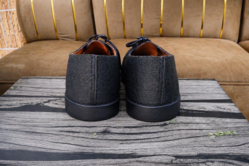 K&ouml;nnte beinhalten: Ein Paar schwarze Schuhe mit einer strukturierten, genarbten Lederoberfl&auml;che und einer glatten schwarzen Gummisohle. Das Innenfutter ist in einem kontrastierenden Beigeton gehalten und die Schuhe haben schwarze Schn&uuml;rsenkel an der Oberseite.