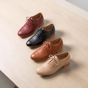 K&ouml;nnte beinhalten: Vier Schn&uuml;rschuhe im Oxford-Stil, die in einer diagonalen Linie angeordnet sind. Die Schuhe verf&uuml;gen &uuml;ber ein Fl&uuml;gelkappen-Design mit dekorativen Brogue-Perforationen und eine strukturierte Lederoberfl&auml;che in Dunkelrot, Schwarz, Braun und Beige.