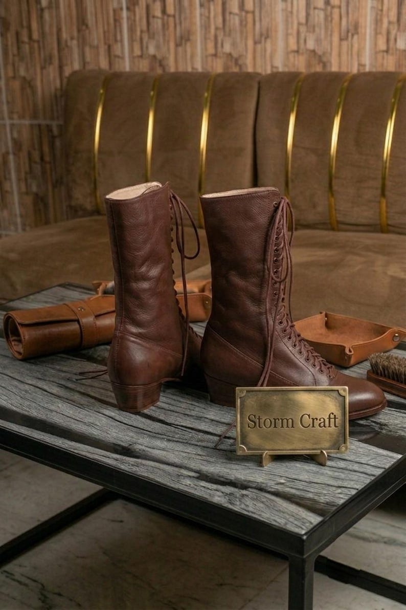 May include: A pair of brown leather lace-up boots with a mid-calf height and a low block heel. A small rectangular brass plaque stands in front of the boots, featuring the engraved text Storm Craft in a serif font, with matching leather accessories.