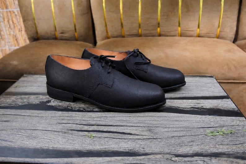 K&ouml;nnte beinhalten: Ein Paar schwarze Schn&uuml;rschuhe mit matter Oberfl&auml;che, abgerundeter Schuhspitze, flachem Absatz und beigefarbenem Innenfutter. Die Schuhe haben ein schlichtes, klares Design mit sichtbaren N&auml;hten an den Seitenteilen und schwarzen Schn&uuml;rsenkeln.