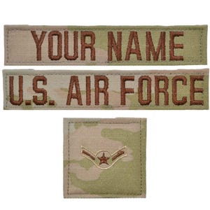 May include: Three rectangular fabric patches with a camouflage pattern in shades of tan, green, and brown. Two long horizontal patches feature embroidered brown text reading YOUR NAME and U.S. AIR FORCE. One square patch displays a brown star emblem.