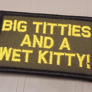 May include: A rectangular olive green embroidered patch with a black stitched border. The patch features the yellow embroidered text "BIG TITTIES AND A WET KITTY!" in a bold, sans-serif font, centered across three lines on the fabric surface.