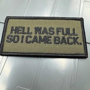 May include: A rectangular olive green embroidered patch with a black stitched border. The patch features the black embroidered text HELL WAS FULL SO I CAME BACK. The design is flat and has a textured fabric appearance with clear, bold lettering.