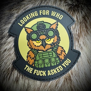 May include: A circular black tactical patch featuring a cartoon owl wearing a green military helmet with night vision goggles and a tactical vest. The text reads LOOKING FOR WHO THE FUCK ASKED YOU in yellow lettering against a pale yellow background.