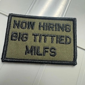 May include: A rectangular olive green embroidered patch with a black stitched border. The patch features the black embroidered text NOW HIRING BIG TITTIED MILFS arranged in three lines across the center of the fabric surface.