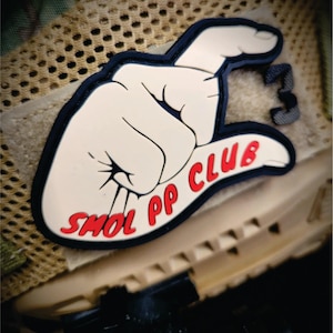 May include: A rubberized morale patch featuring a cream-colored hand gesture indicating a small size, outlined in black. The text SMOL PP CLUB is printed in red letters across the bottom of the hand graphic, with a small black number 3 to the right.