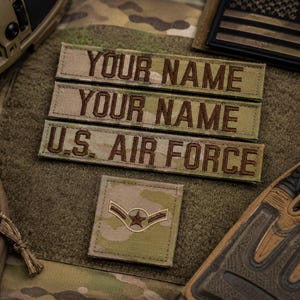May include: Three rectangular patches with camouflage patterns and brown embroidered text reading YOUR NAME, YOUR NAME, and U.S. AIR FORCE, accompanied by a square patch featuring a brown embroidered star and chevron insignia on a camouflage background.