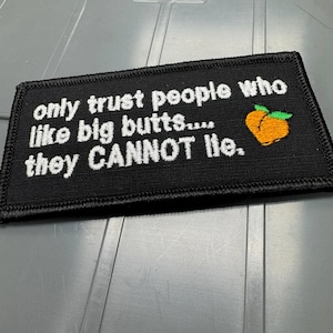 May include: A rectangular black embroidered patch featuring white stitched text that reads, only trust people who like big butts.... they CANNOT lie. To the right of the text is a small, orange, peach-shaped icon with two green leaves.