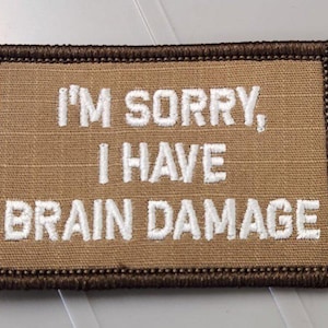 May include: A rectangular tan embroidered patch with a dark brown stitched border. The patch features the white embroidered text "I'M SORRY, I HAVE BRAIN DAMAGE" centered in three lines, utilizing a bold, sans-serif font style throughout the design.