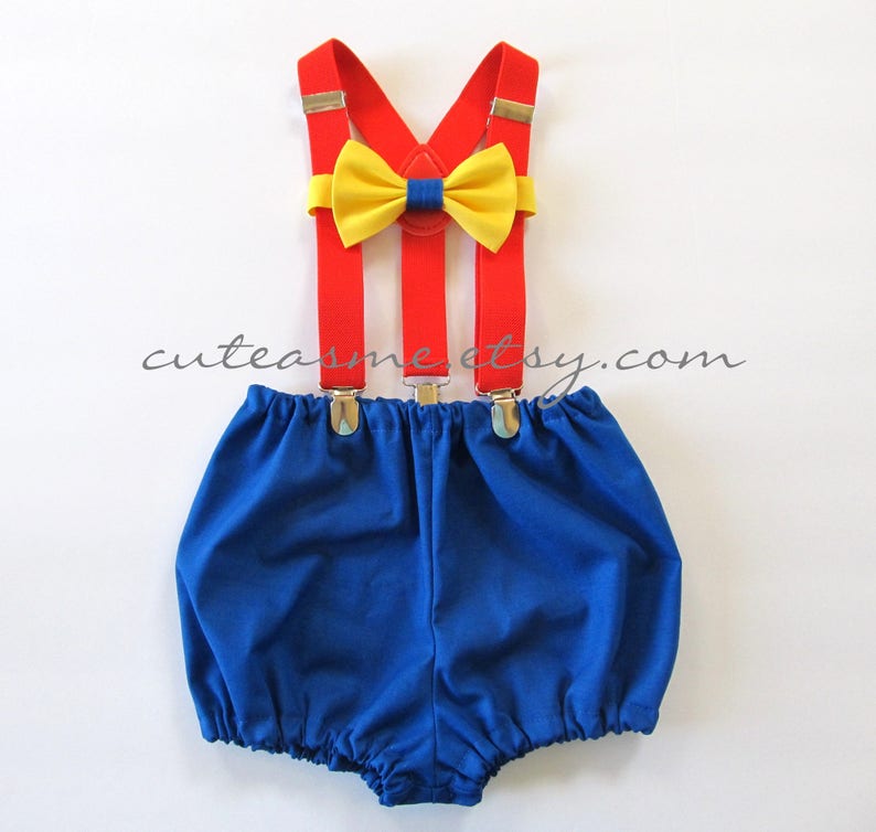 May include: A blue and red baby outfit with suspenders and a yellow bow tie. The outfit is perfect for a baby boy's first birthday.