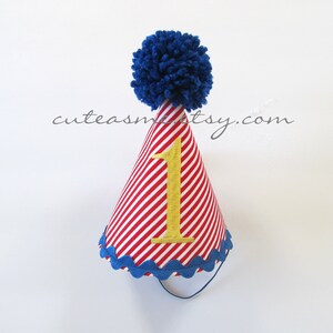 May include: Red and white striped party hat with a blue pom pom on top. The hat has a gold number one on the front.
