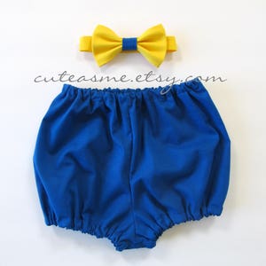 May include: A blue baby bloomer with a yellow bow tie. The bow tie has a navy blue center.