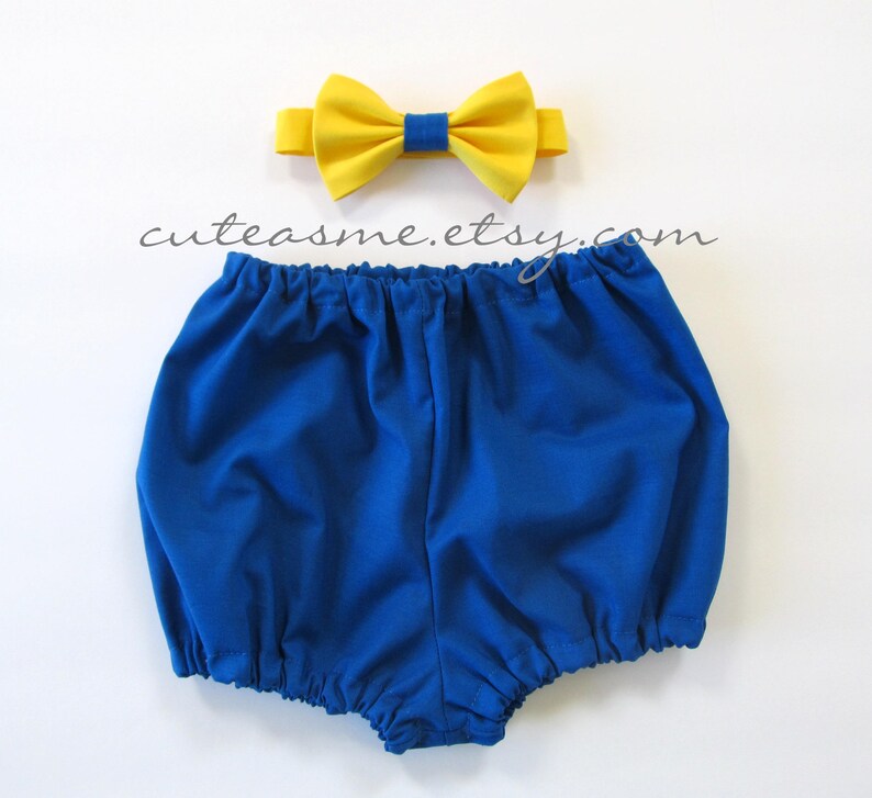 May include: A blue baby bloomer with a yellow bow tie. The bow tie has a navy blue center.