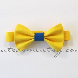May include: A yellow bow tie with a blue center. The bow tie is made of fabric and has a simple design.