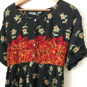 Puede incluir: Vestido maxi negro con estampado floral y una banda floral roja y naranja alrededor de la cintura. El vestido tiene un frente abotonado y mangas cortas. La etiqueta de la marca dice "Whistles".