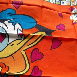 May include: A cartoon duck with blue feathers and a yellow beak is wearing a red heart over each eye. The duck is on an orange background with pink hearts scattered around it.