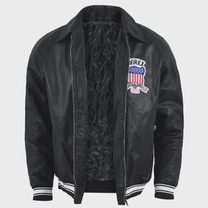 May include: A black jacket with a front zipper closure, a quilted interior lining, and a collar. The chest features a patch with the text "AVIREX ESTABLISHED 1975" and a shield graphic with red, white, and blue stripes. The cuffs and hem have white stripes.