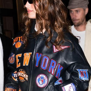 Könnte beinhalten: Eine schwarze Leder-Collegejacke mit zahlreichen gestickten Aufnähern, darunter der Schriftzug NEW YORK in großen orangefarbenen und blauen Buchstaben, verschiedene Logos des Basketballteams New York Knicks, ein Basketball-Motiv und das Wort KITH am Saum.
