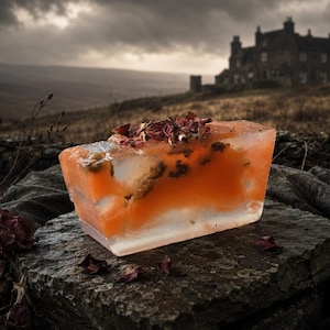 May include: A rectangular block of translucent orange soap embedded with dried rose petals. The soap has a smooth, semi-clear texture with visible floral inclusions throughout the body and a cluster of dried rose petals on the top surface.