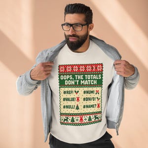 May include: A cream-colored sweatshirt featuring a festive holiday-themed graphic with red and green patterns. The text reads: OOPS, THE TOTALS DON'T MATCH, followed by spreadsheet error codes like #REF!, #NUM!, #VALUE!, #DIV/0!, #NULL!, and #NAME?.