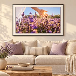 May include: A framed landscape wall art print featuring a vibrant purple lavender field under a bright sun, displayed above a beige sofa with matching throw pillows, a cream-colored throw blanket, and a vase of fresh lavender on a wooden table.