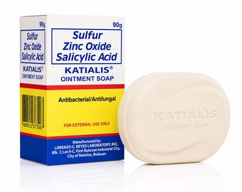 May include: A 90g bar of Katialis ointment soap with a smooth, off-white oval shape and the brand name embossed on the front, displayed next to its rectangular cardboard box featuring blue, yellow, and red text detailing ingredients and usage.
