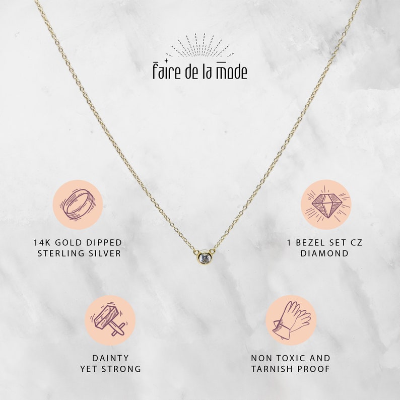May include: A delicate gold-colored necklace with a single bezel-set CZ diamond pendant. The necklace is labeled "faire de la mode" and is described as 14K gold dipped sterling silver, dainty yet strong, and non-toxic and tarnish proof.
