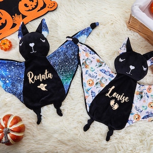 Puede incluir: Dos juguetes de peluche con forma de murciélago, cabezas de terciopelo negro y ojos cerrados bordados. Uno tiene alas con patrón de galaxia azul, el nombre Renata y un icono de fantasma. El otro tiene alas con motivos de Halloween, el nombre Louise y huellas.